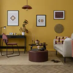 Soggiorno con pareti giallo ocra e accenti tortora. Un divano beige con cuscini colorati e una coperta arancione.