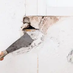 Mano con spatola che rimuove detriti per preparare il muro a come riempire un grosso buco.