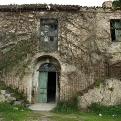 Antica casa in Sardegna, ricoperta di edera, con scale esterne arrugginite e porta verde aperta. Un sogno per chi cerca case a 1 euro.