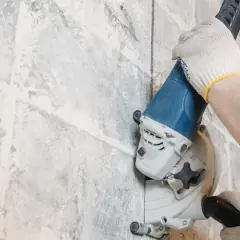 Mani guantate usano una fresatrice per creare tracce nel muro senza polvere, un lavoro di precisione.