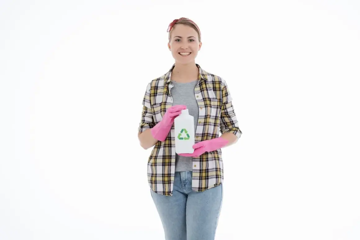 Donna con guanti rosa tiene una bottiglia bianca con simbolo riciclo, forse contiene soda caustica per pulizie ecologiche.